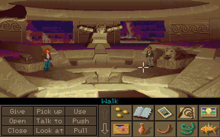 An overhead view of a sandy temple interior with beige stone walls and purple-blue banners. Two pixel-art characters stand in the central chamber near stepped platforms and architectural features. The interface bar at the bottom displays verb commands (Give, Pick up, Use, Open, Close, Talk to, Push, Look at, Pull) and an inventory grid showing various item icons. The art style features low-resolution sprites against detailed background scenery with warm earth tones and decorative geometric patterns along the upper walls.
