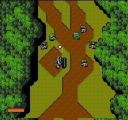 A top-down military strategy view displays a tank positioned in the center of a brown dirt road surrounded by green forest terrain. The road branches into multiple paths forming a cross-like pattern. Several enemy tanks appear as small sprites scattered across the landscape at various positions. A red health bar is visible in the lower-left corner of the screen. The graphics use a limited 8-bit NES color palette with distinct green, brown, and tan hues creating clear terrain delineation.