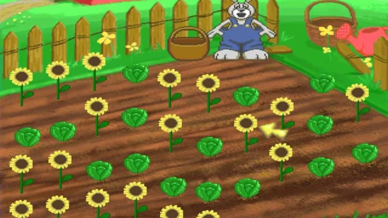 A garden scene featuring a white anthropomorphic character in a blue outfit standing on a wooden platform in the center background, with a brown basket beside it. The foreground contains a tilled brown garden bed scattered with yellow sunflowers and green cabbage plants. A wooden fence with horizontal rails forms the background, decorated with additional baskets and flowers. The scene uses bright green grass, early 1990s pixel art style, and simple geometry typical of educational children's software.