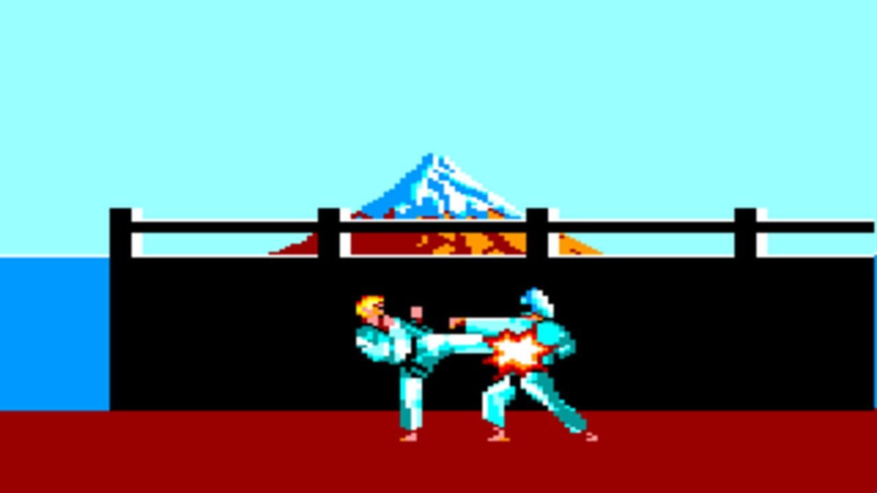 Two cyan-colored martial artists face each other in mid-combat on a red floor against a black building structure. The left figure performs a high kick with yellow and white impact effects, while the right figure blocks with an orange and yellow explosion burst between them. A blue ocean occupies the left edge, and a snow-capped mountain peak in blue and white sits centered in the light cyan sky above a black wooden fence rail. The pixel art uses a limited color palette typical of 1980s arcade fighters.