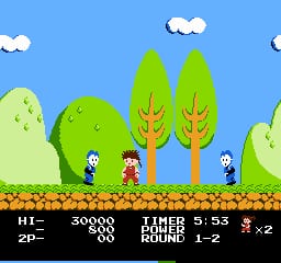 A side-scrolling platformer scene displays a character sprite in red and white standing on a brown brick platform in the center, flanked by green trees and bushes under a bright blue sky with white clouds. The HUD at the bottom shows a black bar with white text reading "HI-2P-", score values "30000" and "700", timer display "5:53", "ROUND 1-2", and a "×2" multiplier indicator. Two additional character sprites appear near the trees on either side of the stage.