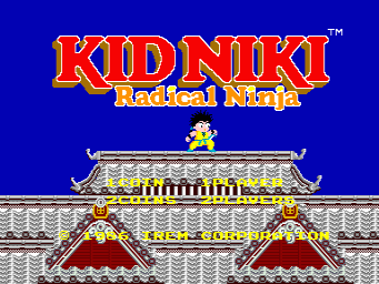 The title screen displays "KIDNIKI Radical Ninja" in large red and yellow pixelated letters against a blue background. Below the logo sits a small yellow ninja sprite positioned on top of an ornate Asian-inspired building structure with gray tile patterns, red roof sections with curved edges, and yellow decorative bands. The architecture features symmetrical design with two prominent red roof peaks flanking the center of the building facade.
