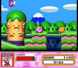 A large green Kirby with an angry expression dominates the left side of the screen, appearing as a copy ability form. The background shows a bright blue sky with white clouds, green grass, and pink wavy terrain. A smaller pink Kirby and orange projectile appear in the mid-ground. The bottom displays a UI bar with Kirby's portrait on the left, a health or ability meter in the center, and score information reading "SCORE: 1180" with "00" displayed in an orange box on the right. The sprite artwork shows SNES-era pixel graphics with limited animation frames visible.