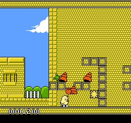 A small pixelated character stands on a yellow brick platform in the center-left of the screen. Above and to the right are stacked yellow brick blocks forming a wall structure with darker outlined edges. Two red objects sit on lower platform ledges. The left side shows a blue sky with a white cloud against a light blue background. A green fence railing appears at the bottom left. The score display reads "0000500" at the bottom of the screen. Black borders frame the top and bottom of the gameplay area.