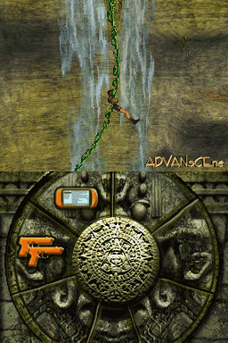 A top-down view displays an ornate circular stone dial or mechanism with a carved face at its center. Hanging chains drape down from above, and a small handheld device with a blue screen sits in the upper left corner of the interface. An orange pistol icon appears on the left side. The background shows weathered stone walls and architecture in brown and gray tones. "ADVANSCe" text is visible in the upper right corner. The overall visual style is consistent with Nintendo DS graphics, featuring limited color depth and pixelated textures.