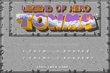 The title screen displays "LEGEND OF HERO TONMA" in large yellow and purple pixelated letters at the top against a textured gray background. Below the logo are two menu options in white text: "1 COIN 1 PLAYER" and "2 COINS 2 PLAYERS". At the bottom, copyright text reads "1989 IREM CORP". The overall visual style uses low-resolution sprite graphics typical of late-1980s arcade games, with a monochromatic checkered pattern forming the background texture.