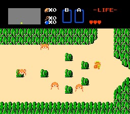 The HUD displays at the top left show a map window and inventory icons for bombs and a key, with three red hearts representing health on the right. The main play area shows a sandy clearing bordered by tall green grass on all sides. A small green-clothed player character stands centrally, surrounded by approximately eight brown enemies with yellow accents scattered across the sand. The sprite art uses a top-down perspective with limited color palette typical of NES-era games.