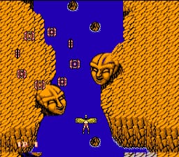 A vertical-scrolling shooter displays two golden winged warrior sprites positioned on the left and right sides of the screen against a blue waterway bordered by orange terrain. A small cross-shaped player aircraft flies down the center channel between the enemies. Multiple golden horned enemy heads float across the upper and middle sections of the screen, with round golden orbs scattered throughout. The 8-bit pixel art uses a limited color palette of blue, orange, gold, and yellow against a solid background.