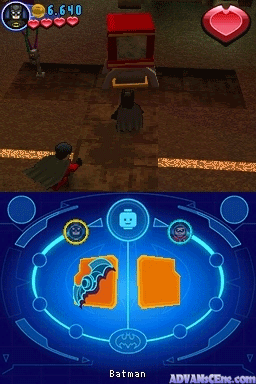 The top screen displays a third-person perspective of Batman standing in a brown-tiled room with wooden furniture and a red chair, with a pink heart icon in the upper right and resource counters at the top left. The bottom screen shows a blue interface menu with Batman's portrait on the left side and two large orange rectangular panels in the center, surrounded by circular selection icons connected by cyan circuitry lines, with "Batman" text centered at the bottom.