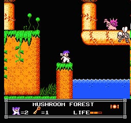 A side-scrolling platformer level titled 'Mushroom Forest' displays a small blue sprite character standing on a tan mushroom platform in the center-right area. Orange and tan colored terrain forms the level architecture with green grass tufts at edges. Two green orbs float in the upper left. A white owl-like creature perches on a platform to the right. Blue water fills the bottom portion of the screen. The HUD shows 'Mushroom Forest' text on the left with life counter and numerical display on the right, set against a black background. Pixel art uses a limited color palette typical of NES-era graphics.