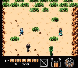 A top-down desert environment features the player character in blue positioned center-left, surrounded by scattered green cacti and brown bushes against tan sand. Two enemy figures in dark clothing stand in the middle distance. The right edge shows a brown rocky cliff wall. The bottom UI displays a health bar of white segments on the left, a map icon, item/weapon icons in the center, and a circular compass on the right. The scene uses 8-bit NES-era pixel graphics with a limited color palette of greens, browns, tans, and blues.