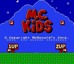 The M.C. Kids title logo appears in large red letters against a blue cloudy sky background with small white stars scattered throughout. Below the title, a copyright notice reads "© Copyright McDonald's Corp." in white text. Two player indicators labeled "1UP" and "2UP" sit in the bottom corners above a green grass ground with a dotted pattern. Small golden square icons flank the upper sides of the screen, rendered in the NES's 8-bit sprite style with a limited color palette of blue, red, yellow, white, and green.