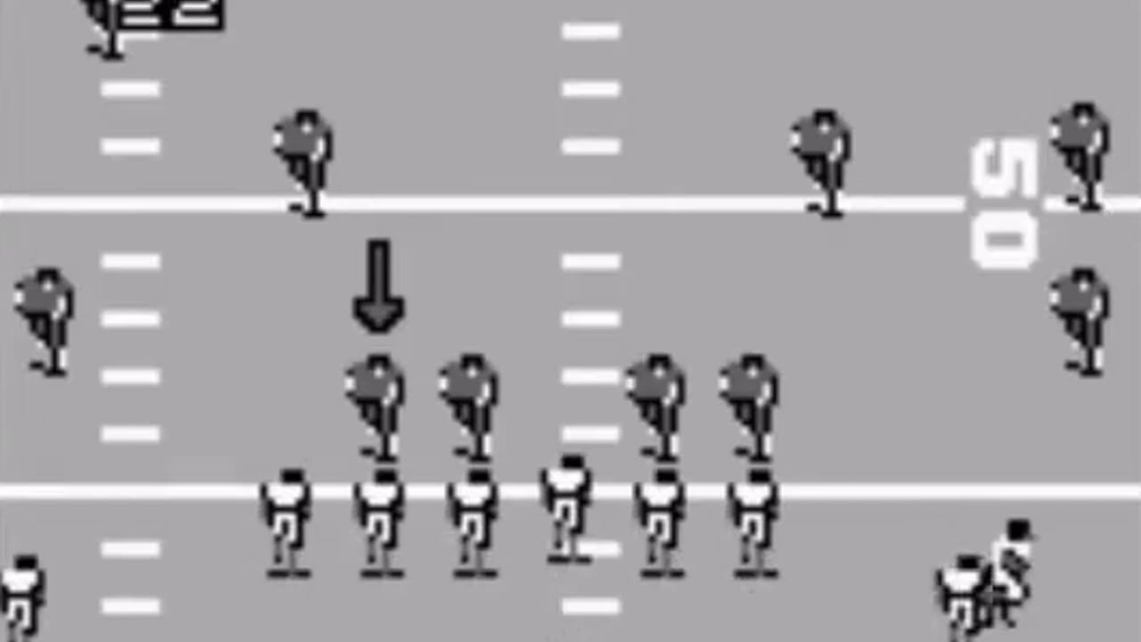 A football field layout displayed in overhead view with two teams of pixelated player sprites positioned across three horizontal white yard-line markers. The upper section shows defensive players in dark uniforms spread across the field with a downward arrow indicating play direction. The lower section displays offensive players in white uniforms lined up in formation. Additional player figures stand on the sidelines at left and right edges. A score display reading '50' appears in white text on the right side. The graphics use a monochromatic gray background with black and white sprite details typical of Game Boy hardware.
