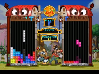 A Tetris game board dominates the center with falling colored blocks stacking in two vertical columns separated by a central divide. Above the play areas sits a ornate archway structure with a golden emblem displaying the word "SCORE" flanked by decorative lion-head gargoyles. Below the score display are cartoon characters and the text "MAGIC GENIUS" in a stylized banner. The left and right sides show stacks of placed Tetris blocks in bright colors—blues, reds, yellows, and magentas—against a dark background. The top features a bright blue sky with purple clouds visible behind the structure. A grassy field and small decorative plants frame the bottom edges of the game interface.