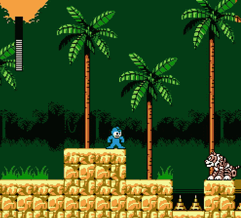 A blue Mega Man sprite stands on tan brick platforms in a tropical jungle level with four brown-trunked palm trees and green fronds against a dark green background. Black silhouetted bushes form the terrain baseline. A white enemy robot appears on the right platform. An orange brick structure labeled with yellow text sits on the left platform. Two small spike obstacles are visible on the ground level. The top-left corner shows part of an orange and black object, possibly a UI element or level hazard.