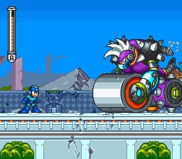 Mega Man stands on a white platform in the lower-left, facing right, while a large purple and black robot with spinning wheels and mechanical attachments moves across the upper-right portion of the screen. The background shows a blue sky and industrial architecture including a tall smokestack and peaked structures. A smaller UI element displaying the number 5 appears in the upper-left corner. The level features tiered white platforms against a green lower section with hanging vines or chains, rendered in SNES-era 16-bit pixel graphics with a bright, saturated color palette.