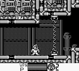 Mega Man stands in the center of a monochrome Game Boy stage, rendered in black and white pixels. The robot master appears in his classic blue-tinted sprite form against a horizontally-scrolling industrial environment with rectangular patterns and architectural elements. The HUD displays Mega Man's health bar at the bottom left and weapon/energy indicators in the top-right corner. The stage background features repeating geometric structures typical of early Mega Man level design, with solid platforms and cylindrical obstacles visible throughout the composition.