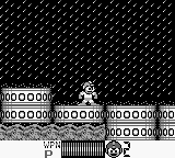 Mega Man stands on a platform in the center-left of a monochrome Game Boy screen, facing right. Above him stretches a grid pattern resembling brick or mesh texture. The HUD displays health and weapon icons in the bottom-left corner, with numerical values visible. Platforms extend horizontally across the screen at varying heights. The sprite palette consists entirely of black and white pixels with minimal color variation, typical of early Game Boy graphics.
