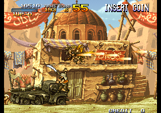 A desert level displays a large domed building in the center background with tan and brown architecture. Military vehicles and equipment sit on platforms in the foreground, including what appears to be a tank on the left side. The pixel art uses a warm color palette of golds, browns, and reds. UI elements show "INSERT COIN" in the upper right, a score display at the top left reading "METAL" with numerical values, and "CREDIT 0" in the lower right corner. The scene uses parallax layering with the background structure elevated above ground-level platforms.