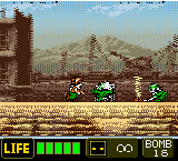 A side-scrolling action scene displays a player-controlled character on the left firing at enemies across a sandy desert landscape. Two small enemy units are visible in the center-middle ground. A large snow-capped mountain dominates the background under a light blue sky. The HUD shows a green health bar, ammunition counter, and score display in the bottom-left corner. Low-resolution pixel art and a brown wooden structure appear on the left edge. The visual style uses a limited color palette typical of early 2000s handheld gaming.