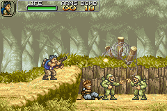 A soldier in blue uniform stands in the foreground of a jungle environment with tan wooden fortifications and sandbag barriers visible ahead. The background shows dense green foliage with parallax depth. The HUD displays health and ammunition counters in the upper left, with a score readout in the upper right. Pixelated sprite-based graphics typical of GBA-era action games are visible throughout the scene.