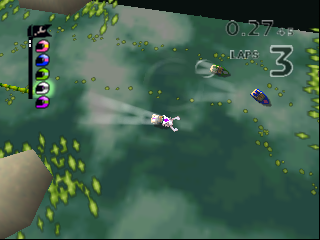 A top-down racing view shows two small toy vehicles on a green terrain with yellow leaf-shaped obstacles scattered across the surface. The left side displays a vertical health or power bar with colored segments in blue and purple. The upper right corner shows a lap counter reading "3" and what appears to be a timer display. The graphical style features low-polygon 3D models with a muted color palette typical of N64-era graphics. Vegetation and terrain details create a miniaturized diorama effect characteristic of the Micro Machines series.