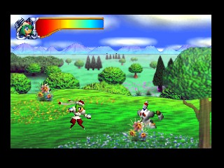 A colorful outdoor scene displays a green grassy field with scattered flowers and multiple trees in the background under a blue sky with white clouds. Three small character sprites occupy the foreground and middle ground on the grass. A blue health or temperature meter appears in the upper left corner. The art style uses bright, solid colors with low-resolution 3D models typical of N64 graphics, and a parallax background shows rolling hills and distant landscape elements.