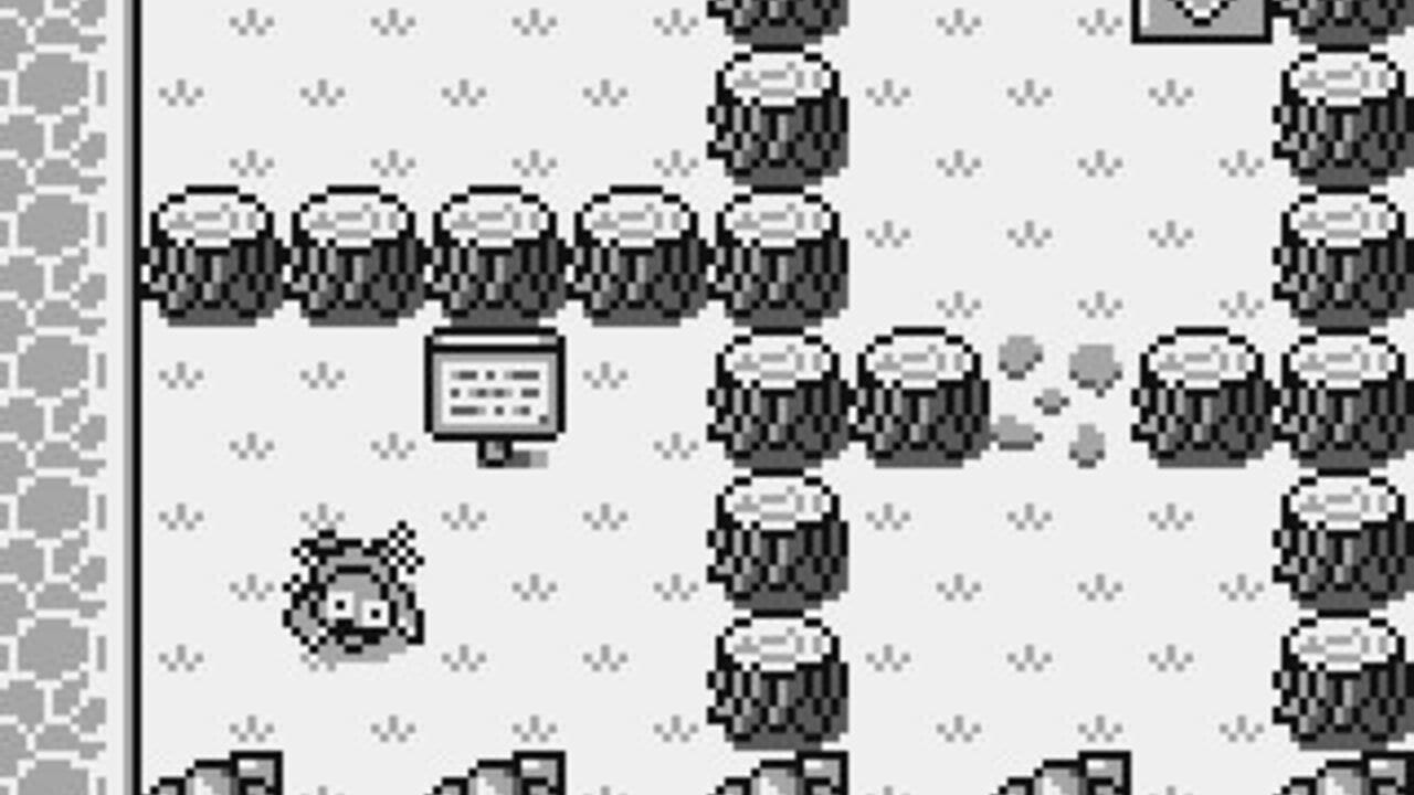A small pixelated mole character with a checkered pattern stands in the lower-left area of a monochrome game screen. Multiple barrel-shaped enemies with textured tops are arranged throughout the stage, with several clustered on the right side and others spaced vertically down the center. A small monitor or sign displaying text sits in the upper-middle area. Gray pixel debris or blocks appear scattered in the middle-right portion. The background is light with small dotted patterns scattered across it, and a brick or stone-textured border runs along the left edge of the screen.
