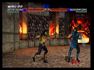 Two fighters face each other in a stone arena with flaming torches on the walls. The character on the left wears black and yellow, while the opponent on the right wears blue. A health bar spans the top of the screen, with "WINS: 00" and "SUBSPECIES" on the left side and "SCORPION" on the right. The arena features brown sand flooring, stone pillars, and large flames visible through an arched doorway in the background. The 3D models show low polygon count typical of late 1990s N64 graphics.