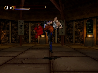 A blue-clad fighter stands in the center of an ornate temple interior, facing two opponents in red and tan clothing positioned above. The scene features richly detailed golden doorways and decorative panels lining the walls. A health bar appears in the upper left corner showing the player character's remaining vitality. The floor displays a shadow beneath the player, and warm amber lighting illuminates the architectural elements in the background.
