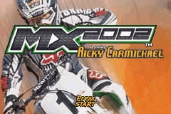 A motocross rider on a dirt bike dominates the left side of the screen, captured mid-jump in a dynamic pose. The 'MX 2002' logo appears in green text with a metallic outline in the upper portion, followed by 'Ricky Carmichael' in smaller white lettering. An orange gradient background fills the right side. A yellow rectangular button or UI element is visible in the lower-right corner. The overall presentation uses a bold, sports-game aesthetic with high-contrast colors typical of early 2000s GBA graphics.