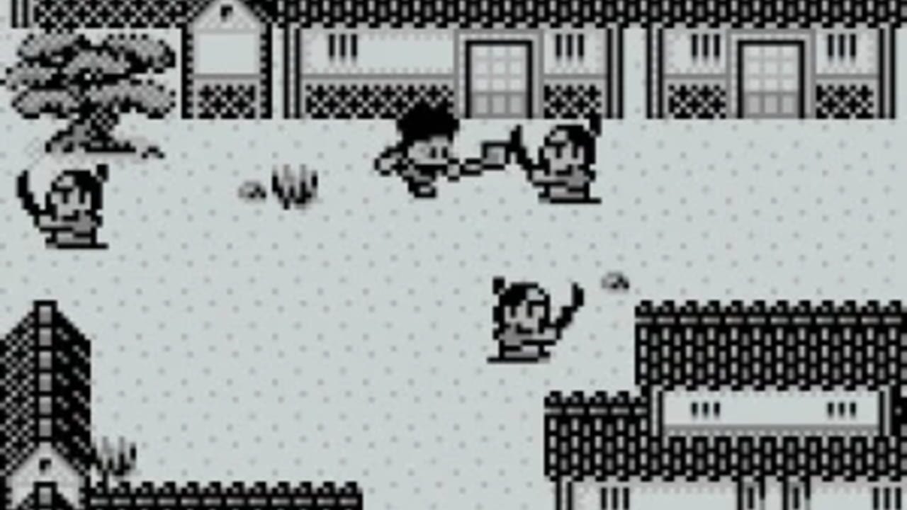 A monochrome Game Boy screen displays a courtyard scene with a brick building featuring latticed windows and doors across the top. A playable character stands in the center-right area of the gravel ground. Four enemy characters with round heads are scattered across the scene—one on the left, two in the upper-middle area, and one in the lower-center. A brick wall structure appears on the left side, and a dark building section is visible on the right. Pixelated sprite graphics use the Game Boy's limited monochrome palette with distinct black and white elements.