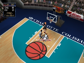 An overhead view of a basketball court with a teal and blue color scheme displays a large red basketball in the center. A player character stands on the court near the basket. The arena features visible sponsorship signage including text reading "COLISEUM" along the sidelines. A scoreboard is visible in the upper portion of the arena. The game UI shows player statistics and options in the top-left corner. The court is rendered with a wooden floor texture and surrounded by crowd elements in the background.
