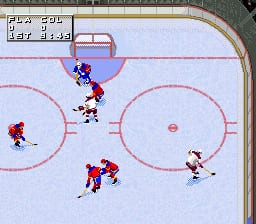 An ice hockey rink viewed from above shows five players in red and white jerseys positioned across the frozen surface. Red players occupy the left and center areas, while a white player stands on the right side near the boards. The rink features three face-off circles marked with pink lines and a center circle. A small score panel in the upper left displays game information. The sprite-based graphics use a light blue ice surface with red and white player sprites rendered in low resolution typical of SNES-era sports games.