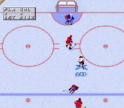 A hockey arena viewed from above shows two teams positioned on the ice. Red and white player sprites occupy the center and lower portions of the rink, with one player in dark red holding the puck near the top. Blue dashed circles mark the offensive zones at both ends, and the goal areas are outlined in pink. A scoreboard at the top displays "PLAY 98" and "For SNES" text. The ice rink features a light blue background with red center line markings and white boards forming the rink perimeter. Small pink dots mark face-off locations.