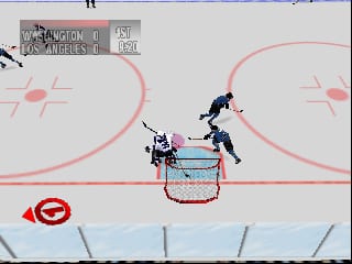 A hockey rink viewed from above shows two player characters positioned near the goal crease, with one player in white and one in dark blue competing for the puck in front of the net. The pink-outlined rink boards frame the play area, with a red circular crosshatch pattern visible in the lower left corner. A scoreboard appears in the upper left displaying team names and score. The low-resolution 3D graphics and flat color palette are typical of N64-era sports games.