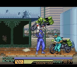 A blue-clad ninja character stands centrally in a street scene, holding a large yellow weapon overhead. To the right, a smaller cyan-colored character operates a motorcycle. The background shows a dark green storefront on the left and a tall striped building on the right, with bare trees visible in the distance. The HUD displays a health bar at the bottom left, a timer reading 39:54 at the bottom right, and the game title at the top left. The sprite work uses a 16-bit pixel art style with distinct color separation typical of SNES-era graphics.