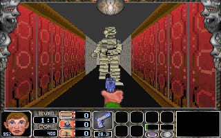 A skeletal figure stands centered in a narrow corridor with red damask-patterned walls extending symmetrically on both sides. The first-person perspective creates a vanishing point toward the skeleton. At screen bottom, a status bar displays the player's face portrait on the left, inventory slots in the center showing various items and ammunition counts, and a black area on the right. A compass icon appears at the top center of the screen. The overall aesthetic is low-resolution 3D rendering typical of early-1990s DOS games, with pixelated textures and flat sprite elements composing the environment.