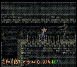 A player character in blue clothing stands on a wooden platform inside a brick-walled dungeon. A skeletal enemy figure appears on the right side. The HUD displays health bars at the bottom in red and green, with a life counter showing 457 and a crystal power indicator at 0. Text windows with dialogue or information occupy the lower portion. The graphics use 16-bit sprite-based visuals with dark brown and gray stone textures forming the background architecture.
