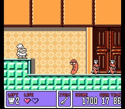 A chef character stands on green platform tiles in the center-left of the scene, facing a large red door on the right side. The background features a beige patterned wall with brown vertical bars at the top and a wooden door frame. The bottom UI displays a purple health bar with two heart icons, a purple item slot icon, and numeric values reading "1100 13 36" in white text. The overall color palette uses orange, green, beige, and red tones typical of early 1990s NES graphics.