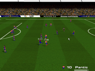 A soccer match viewed from an overhead perspective displays two teams positioned on a green pitch with white boundary lines. Players in red jerseys occupy the left side while blue-jerseted players cluster in the center-right area near the ball. A crowded stadium with yellow-brown spectators fills the background behind blue advertising boards. The UI shows a score of 10-Pantic in the bottom-right corner. The graphics use low-resolution sprites with flat colors typical of early 1990s DOS football simulation games.
