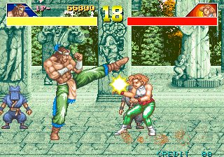 Two muscular fighters engage in combat in a garden setting with stone pillars and foliage visible in the background. The character on the left performs a kicking attack while the opponent on the right recoils. A small blue enemy figure appears in the lower left corner. Health bars for both fighters are displayed at the top of the screen in yellow and red. The sprite-based graphics show detailed musculature and clothing rendered in the arcade fighting game style typical of early 1990s hardware.