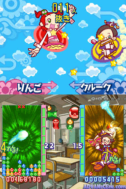 A split-screen gameplay display shows two Puyo Puyo 7 matches on Nintendo DS. The top half features two character portraits—a girl in red on the left and a character in yellow on the right—against a blue sky with white clouds and a decorative pattern. The bottom half displays two active game boards side-by-side with colored Puyo pieces and explosive effects; the left board shows a green burst effect with a score of 22, while the right board displays an orange burst with a score of 15. Score counters appear at the bottom left (0086130) and right (0000545), with Japanese text labels visible above each board.