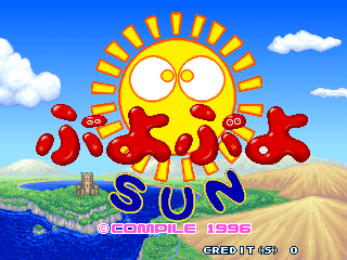 A large smiling yellow sun character with radiating points dominates the center of the screen, surrounded by red Puyo pieces arranged in a scattered pattern. The sun has wide oval eyes and a simple mouth expression. Below the sun, blue text reading "SUN" appears above magenta text stating "COMPILE 1996". The background displays a bright blue sky with white clouds, a landscape featuring green grass, mountains, and blue water, with a castle structure visible in the middle distance. White text reading "CREDIT 1ST 0" appears in the lower right corner.
