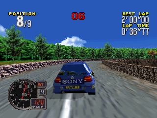 A blue rally car drives down a wide asphalt road lined with stone walls and green trees under a bright blue sky with white clouds. The in-game HUD displays position 9/9 in the upper left, a lap timer showing 2'00"00 at the top center, elapsed time 0'36"77 in the upper right, and a circular speedometer with gear indicator in the lower left. The viewpoint is directly behind the vehicle in third-person perspective.
