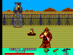 A horizontally-scrolling action game displays a character in red and black clothing positioned in the center-right of a sandy outdoor area with a wooden palisade fence and watchtower structure in the background. The blue sky features pixelated terrain details. The HUD at the bottom shows a score of 000000, a health or ammo counter, a weapon icon, and a numerical value of 60. A small brown object appears in the middle-left of the play area. The sprite-based graphics use a limited color palette typical of early SMS games.