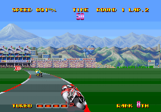 A motorcycle racer in red and white leans into a left turn on a gray asphalt track while approaching a stadium filled with spectators. Mountains and a snow-capped peak dominate the background under a clear blue sky. The HUD displays timer, lap count, rank position, and gear status in yellow text at top and bottom. Pixel art sprites show 16-bit resolution typical of early 1990s arcade racing games, with parallax scrolling visible in the layered mountain scenery.