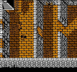 A stone brick wall structure dominates the image, composed of alternating vertical columns of golden-yellow and dark gray bricks arranged in a repeating pattern. The wall extends across the full width with a light gray stone floor visible at the bottom edge. The NES-era pixel art displays a limited color palette with blocky 8-bit sprite resolution typical of early 1990s platform games.
