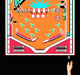 A pinball table viewed from above displays an orange playfield with blue and white bumpers arranged in the upper area. Multiple light-blue arrow projectiles scatter across the field. Two circular scoreboards with numbers appear on the right side. Pink and red flipper zones occupy the bottom corners, labeled with game text. A hand holding a controller is visible at the bottom of the screen, rendered in a dark silhouette style typical of NES-era graphics.