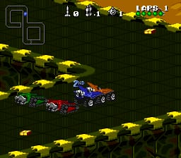 A top-down racing view displays multiple vehicles on a dark green track with yellow-painted sections forming the road borders. Several pixelated cars in different colors—including blue, red, and yellow—are positioned across the track at various distances. The HUD shows "1st: 1" and "LAPS: 1" in the upper right corner, with score indicators visible at top left. Yellow vehicular sprites are scattered around the track perimeter, and the overall scene uses the SNES's 16-bit color palette with a typical Mode 7-style perspective effect common to Mode 7 racing games of that era.